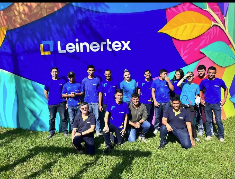 Equipe da Leinertex em frente ao painel da empresa